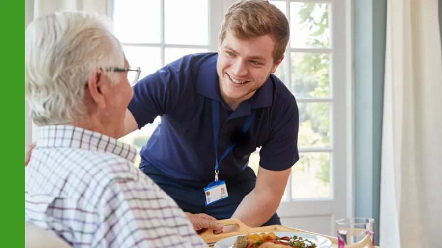 Pflegefachperson serviert einem älteren Mann eine Mahlzeit